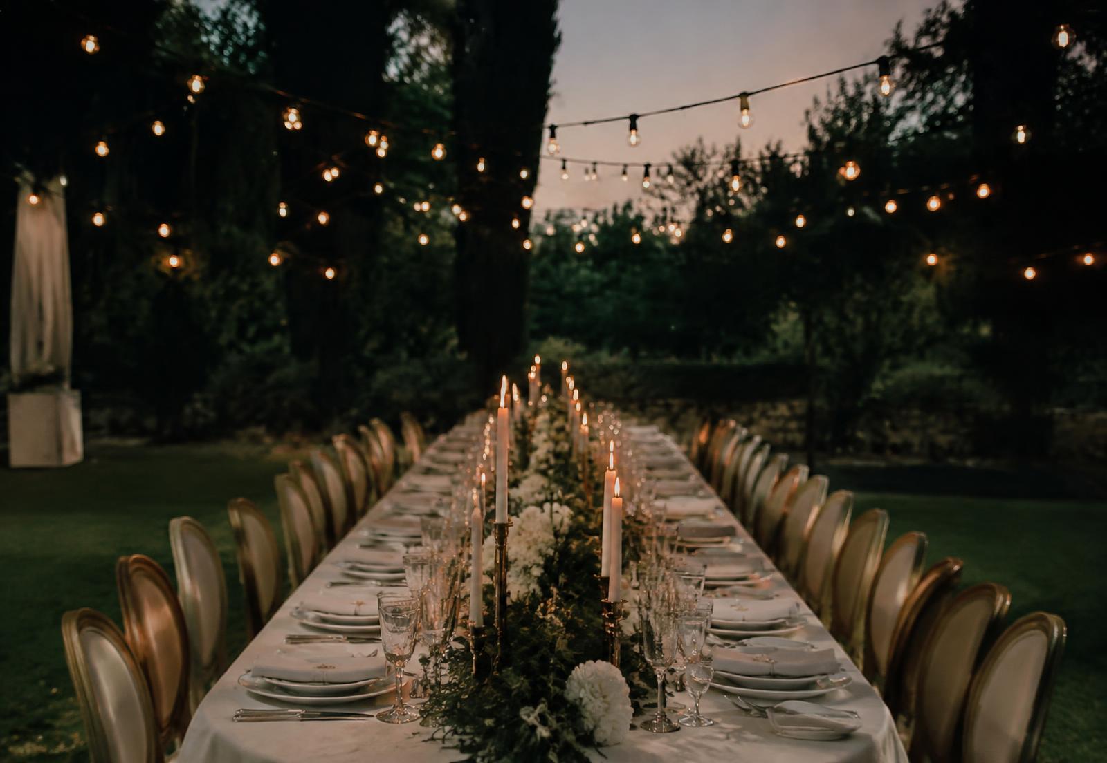 Mesa larga de boda al aire libre con velas y luces colgantes