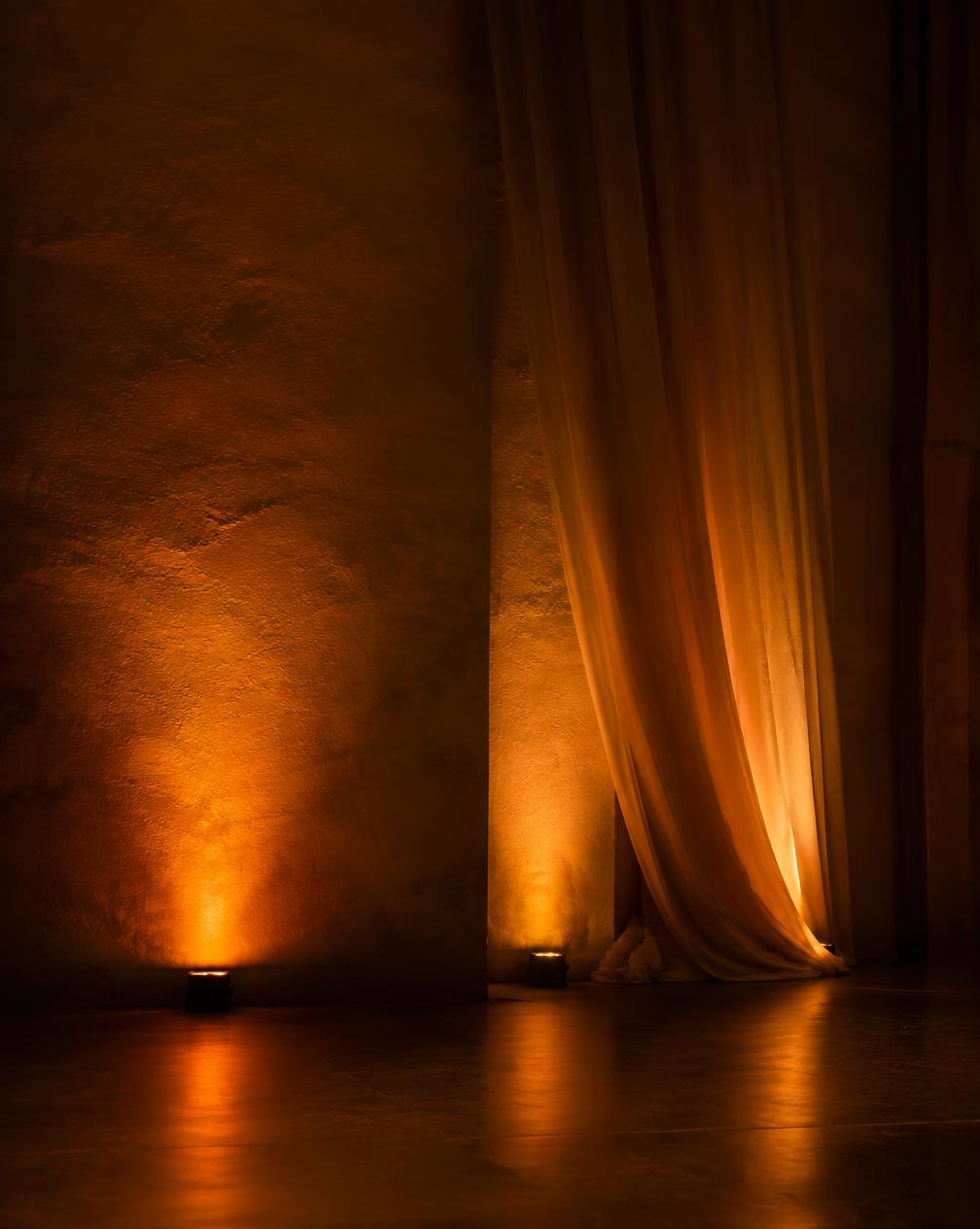 Iluminación ambiental cálida sobre un muro texturizado y telas